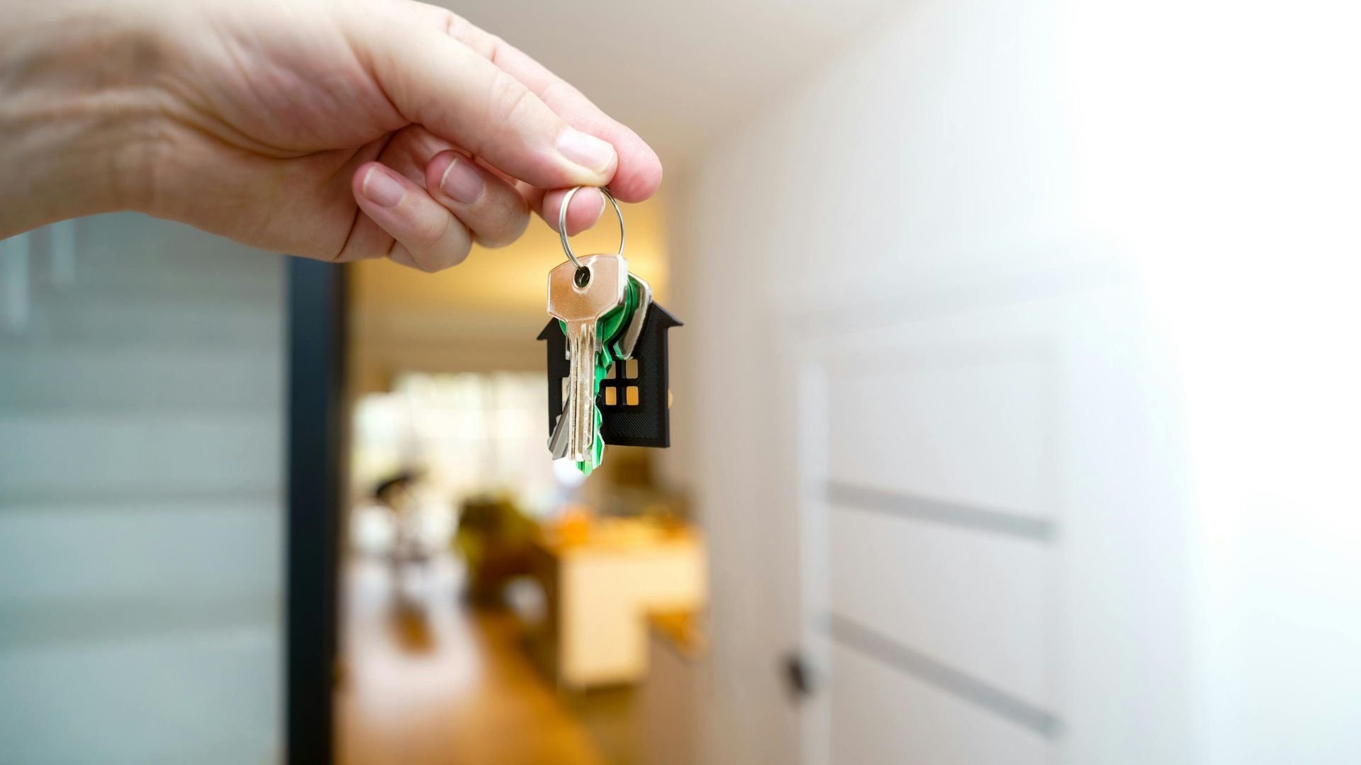 Hand holding house keys with small house keychain in blurred room