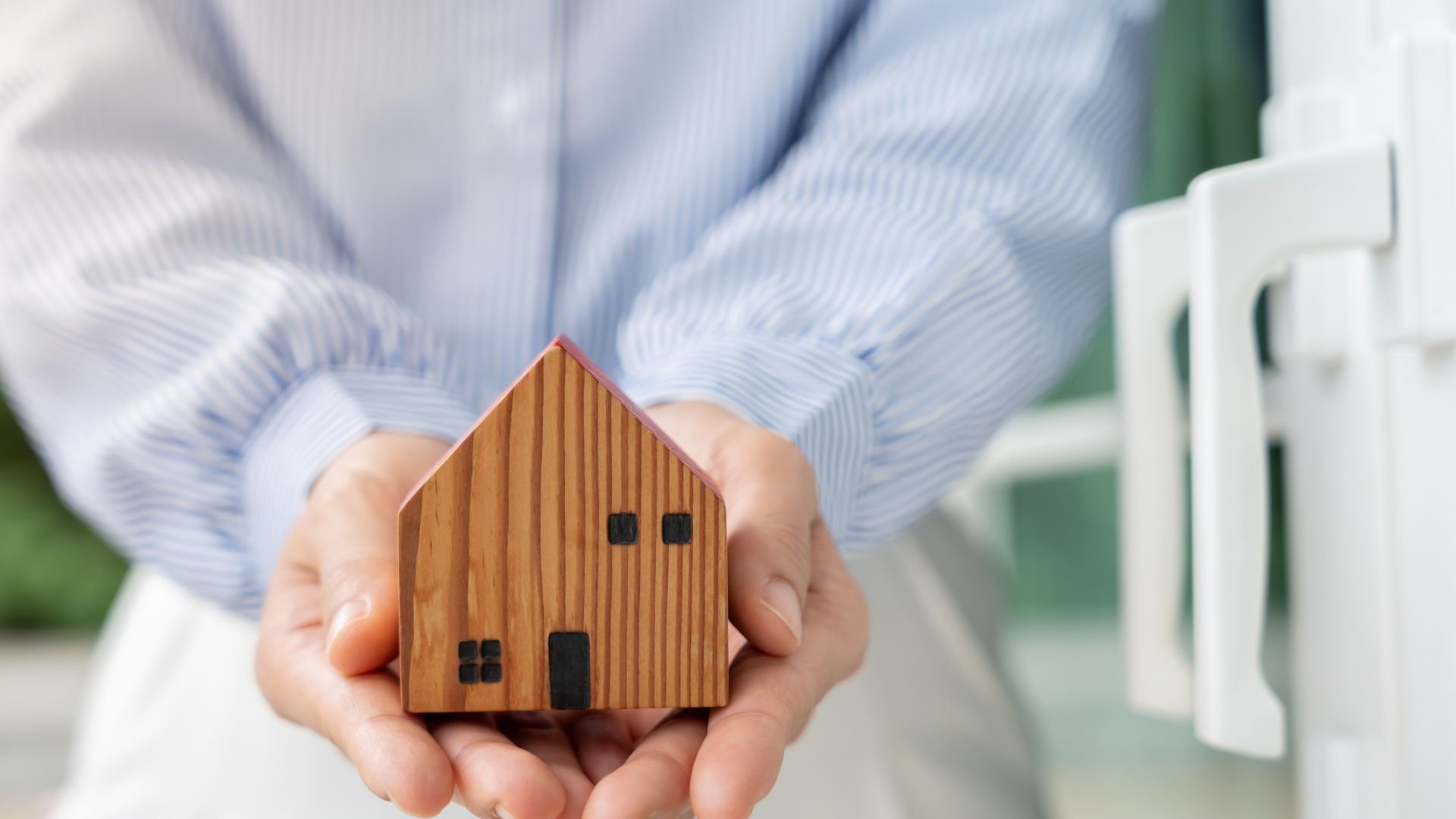 Wooden miniature house held gently in hands, symbolizing home ownership