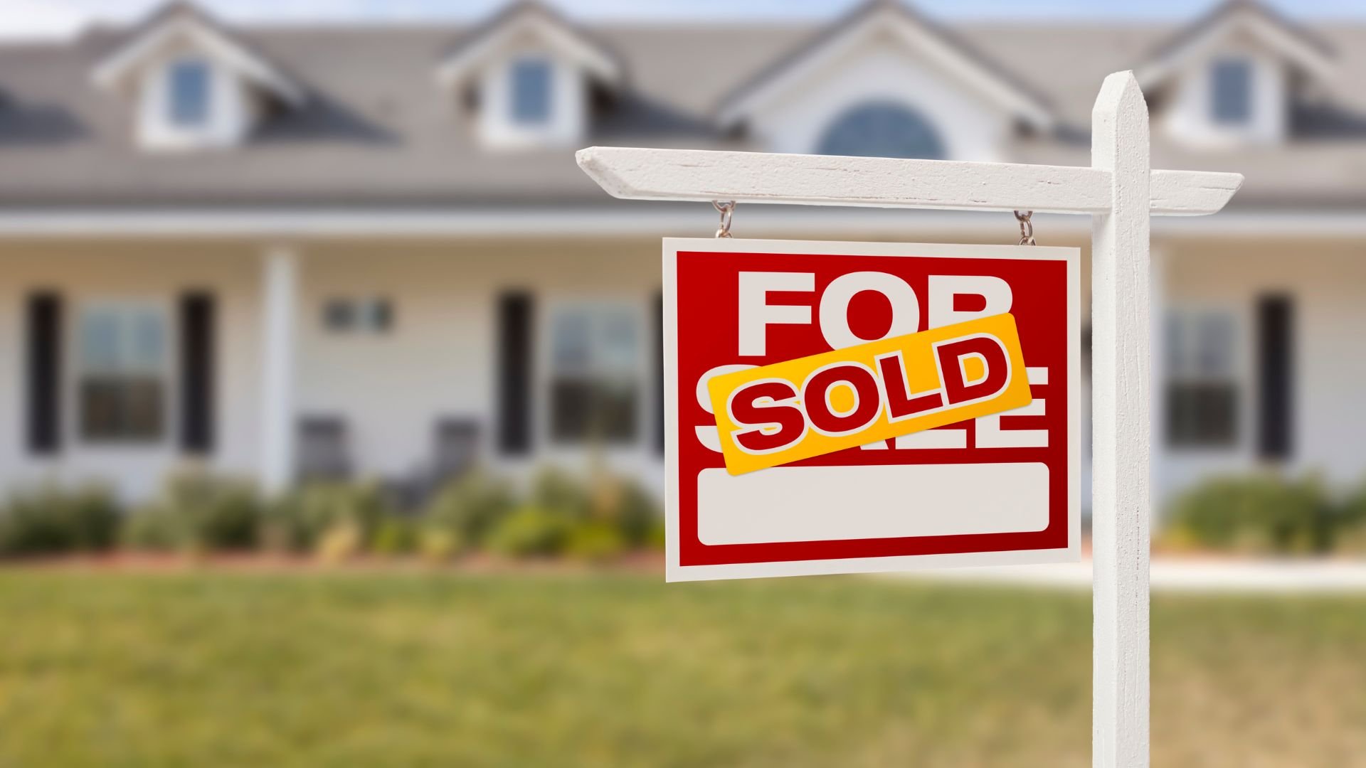 Sold real estate sign in front of suburban house with white exterior