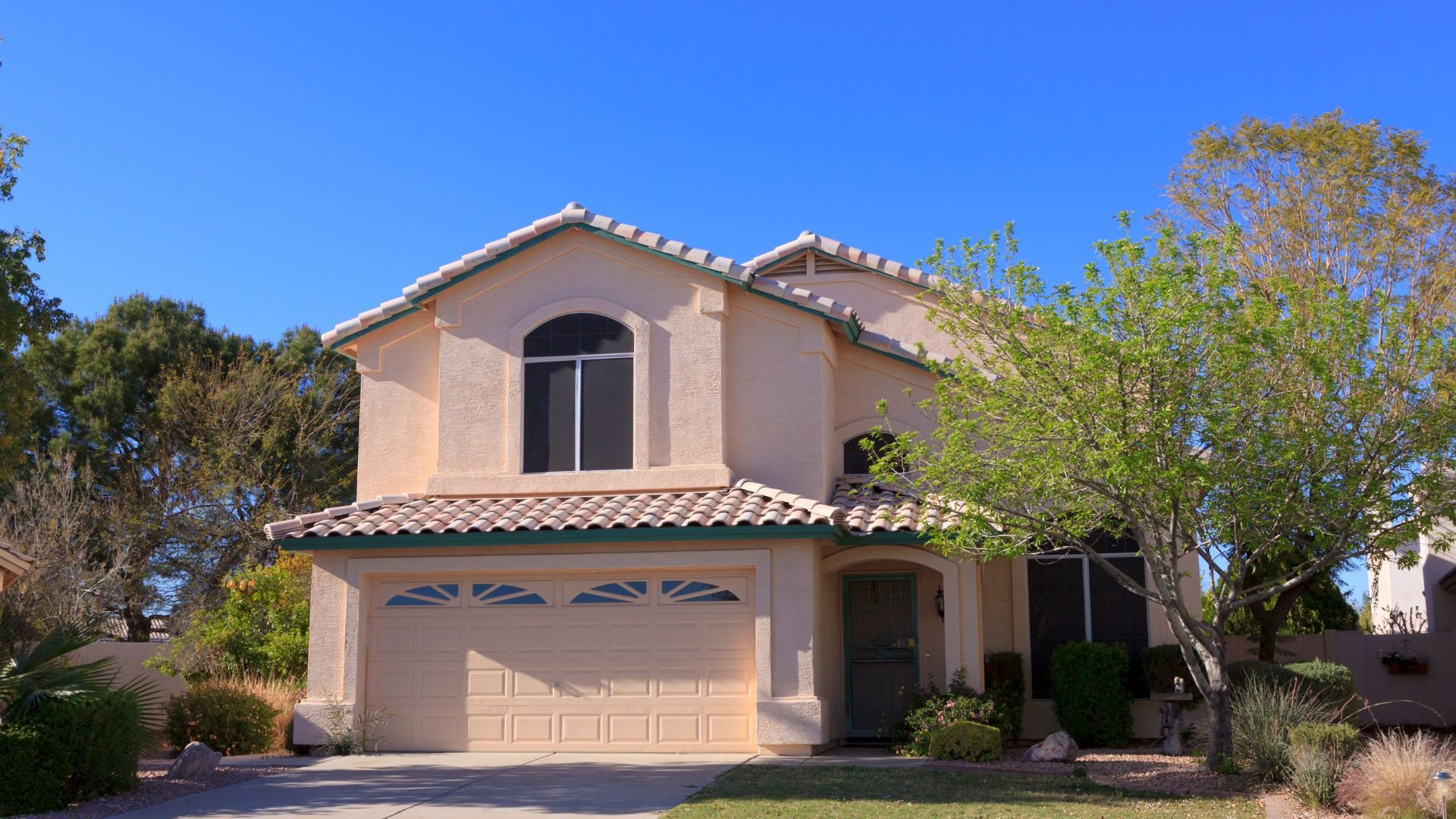 Two-story stucco house with tiled roof and two-car garage on sunny day
