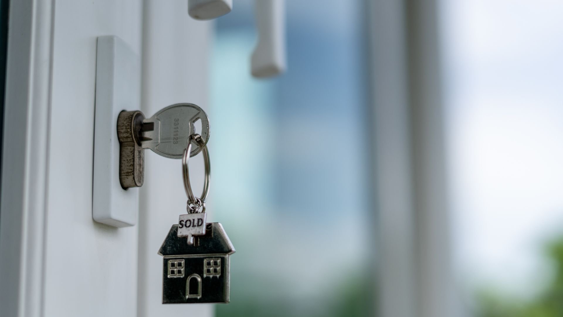 House key with "SOLD" keychain hanging in door lock