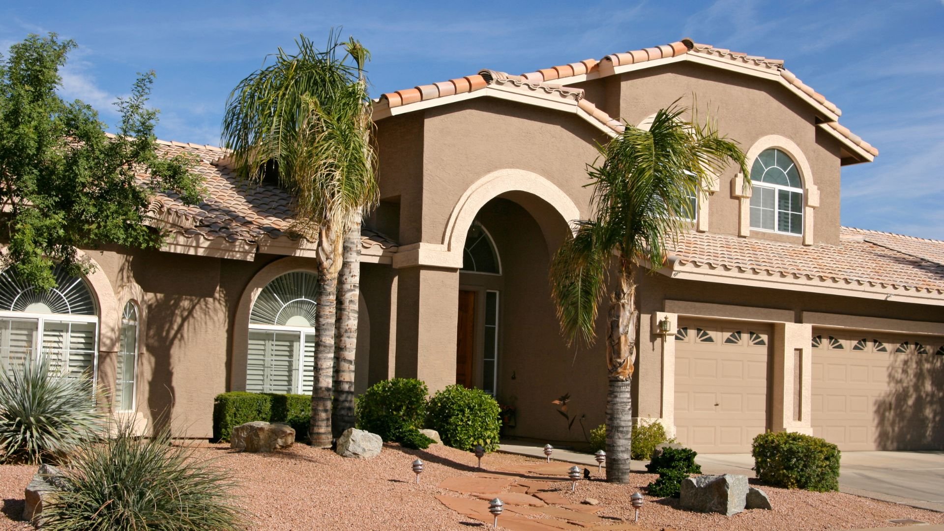 Large stucco house with palm trees and desert landscaping in Southwest style
