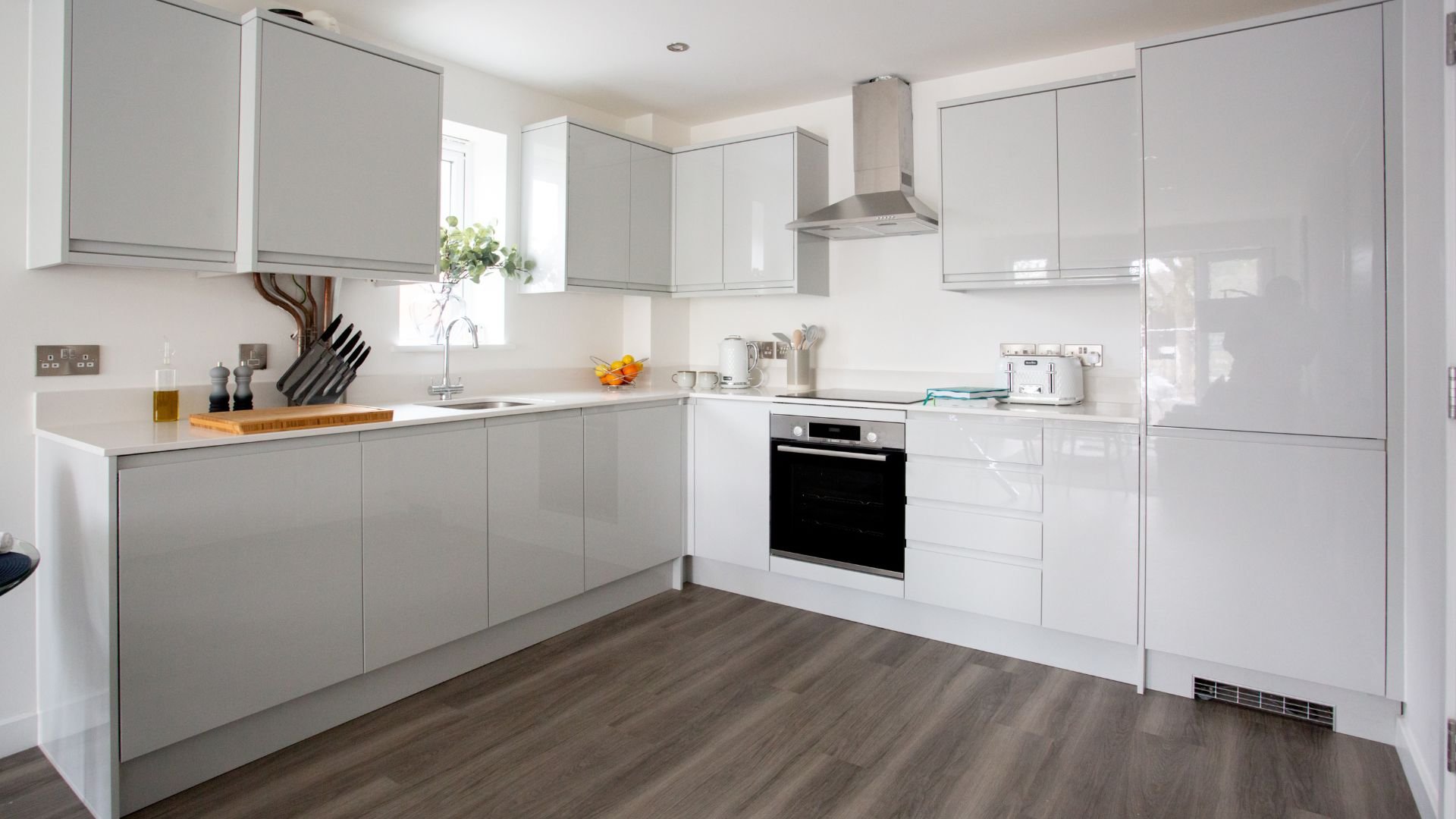 Modern, clean white kitchen with sleek appliances and wooden floor